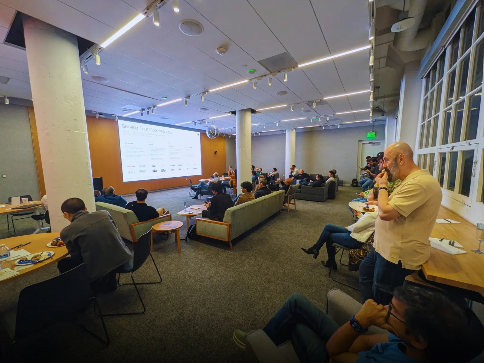 Guests at the previous San Francisco NetSuite user group watching a session on a projector screen from couches and tables, hosted by Stacksync